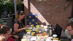 A group of people dining at an outdoor table with various breakfast items and a brick wall in the background.