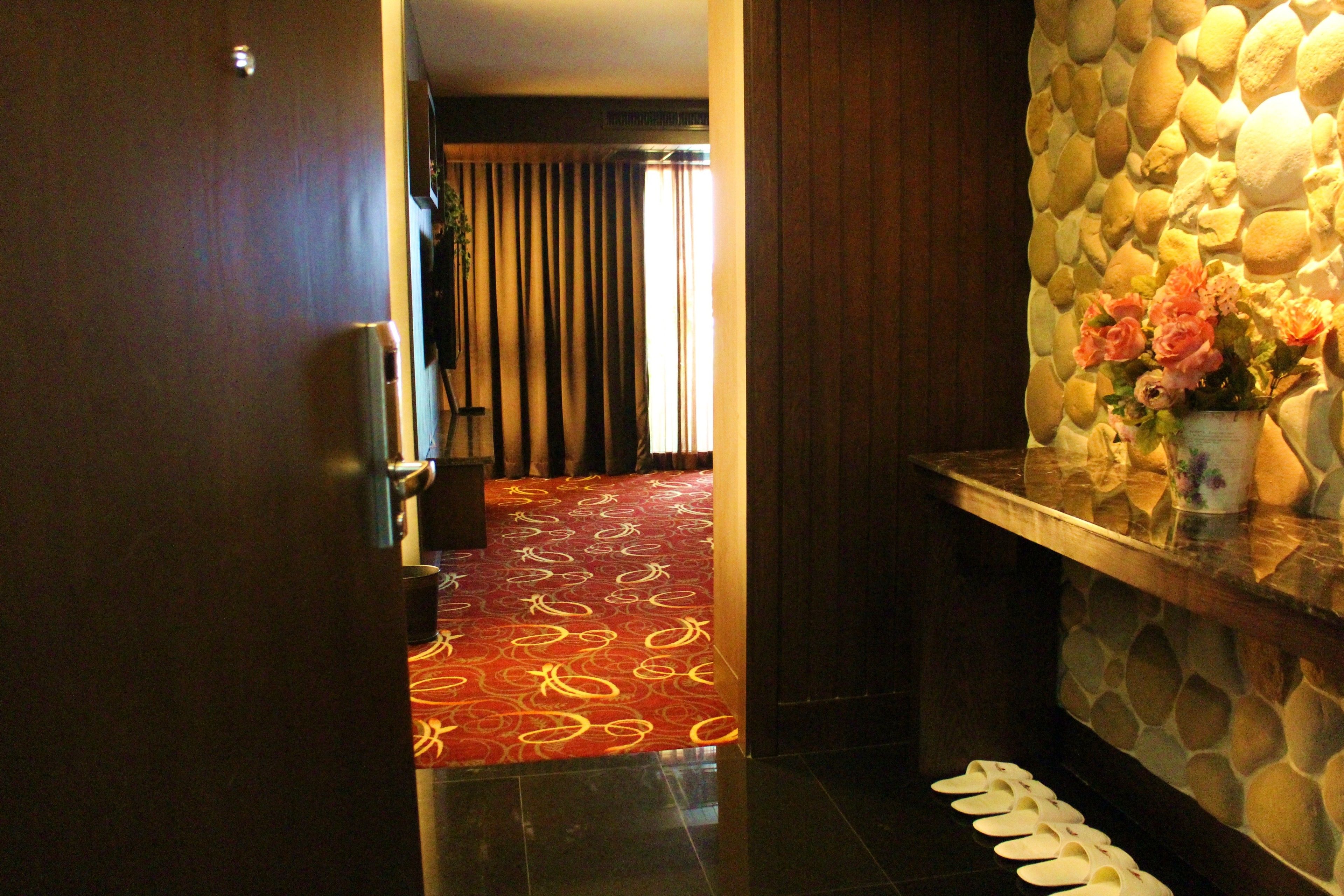 A hotel lobby with a stone wall, a red carpeted area, and a vase of flowers on a counter.