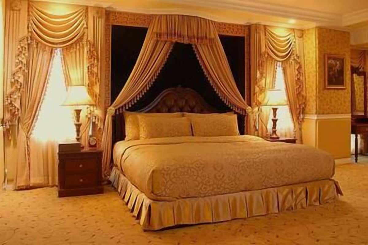 Una cama grande y elaborada con dosel, dos mesitas de noche con lámparas y suelo cubierto de alfombra.