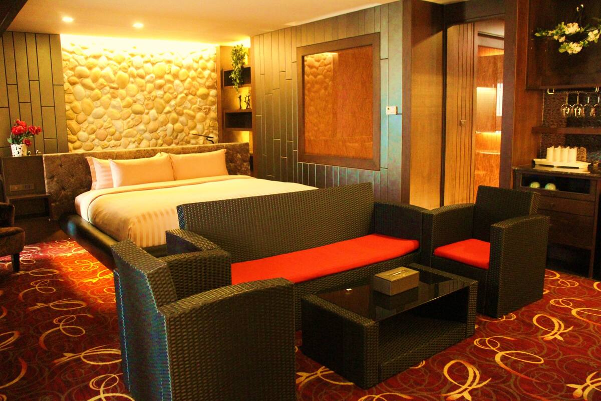 Habitación de hotel con una cama grande, un sofá, una mesita de centro y una pared de piedra.