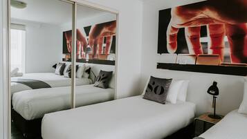 Habitación de hotel con dos camas individuales, un espejo grande y obras de arte en la pared.