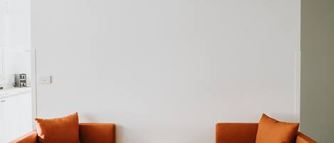 A room with two orange armchairs, a small wooden table, and a white air conditioning unit mounted on the wall.