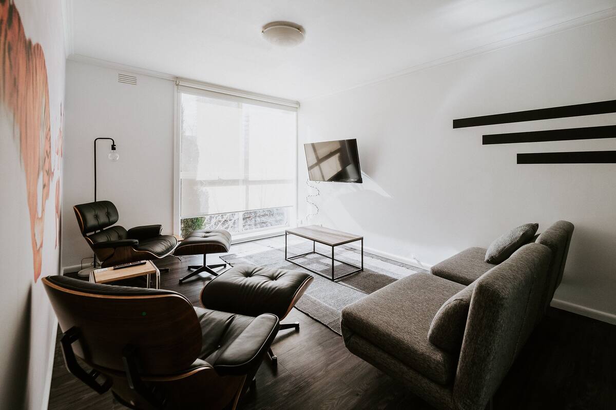 A modern living room with a sofa, chairs, a coffee table, and a TV mounted on the wall.