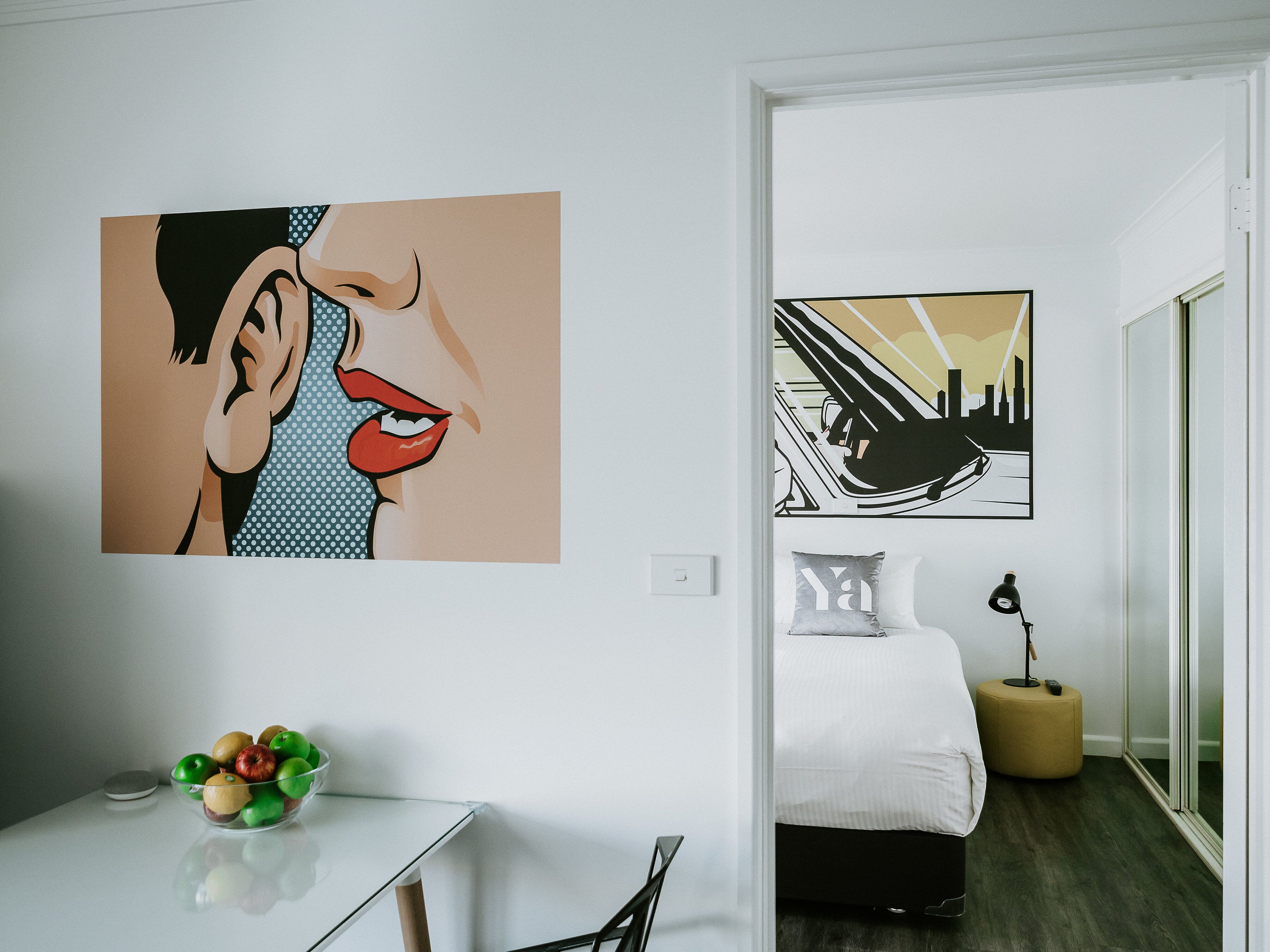 Ein modernes Hotelzimmer mit einem Bett, einem Nachttisch mit Obstschale und zwei Kunstwerken an den Wänden.