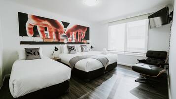Habitación de hotel moderna con dos camas, un sillón de cuero negro, un ventanal grande y un televisor de pared.