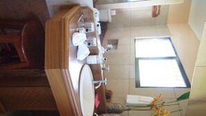 Un bany amb un moble de tocador de fusta, un lavabo i una finestra que deixa entrar llum natural.