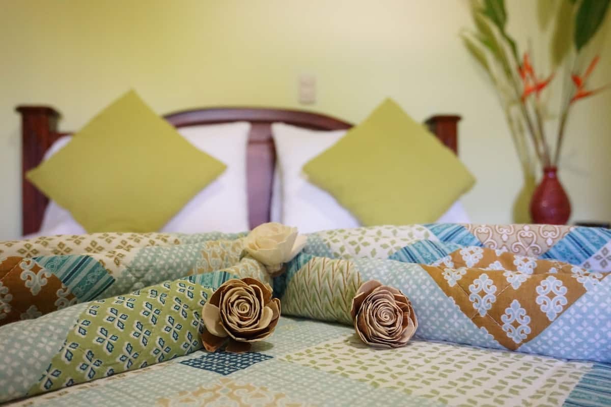 A neatly made bed with patterned bedding and decorative pillows, a wooden headboard, and a vase with flowers in the background.