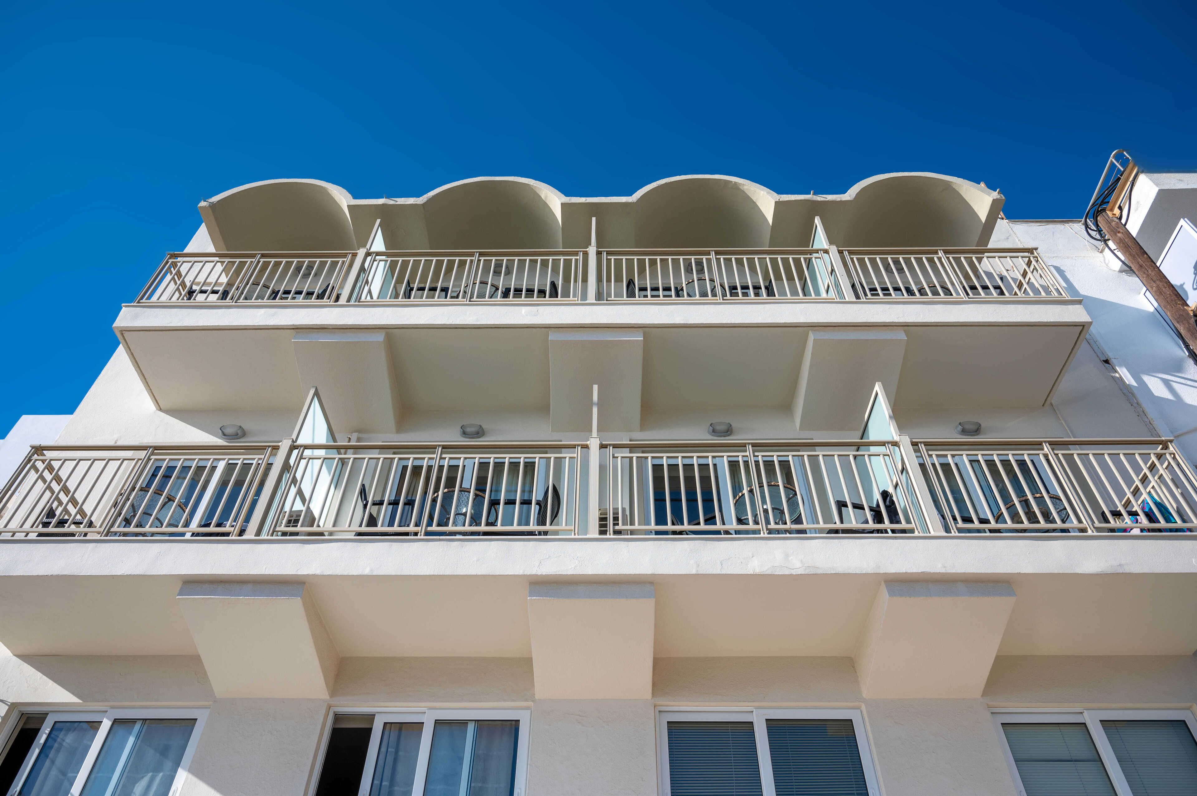 Un immeuble à plusieurs étages doté de balcons, de grandes fenêtres et surplombant un ciel d’un bleu éclatant.
