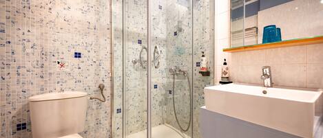 A bathroom with a glass-enclosed shower, a toilet, and a sink with a mirror above it.