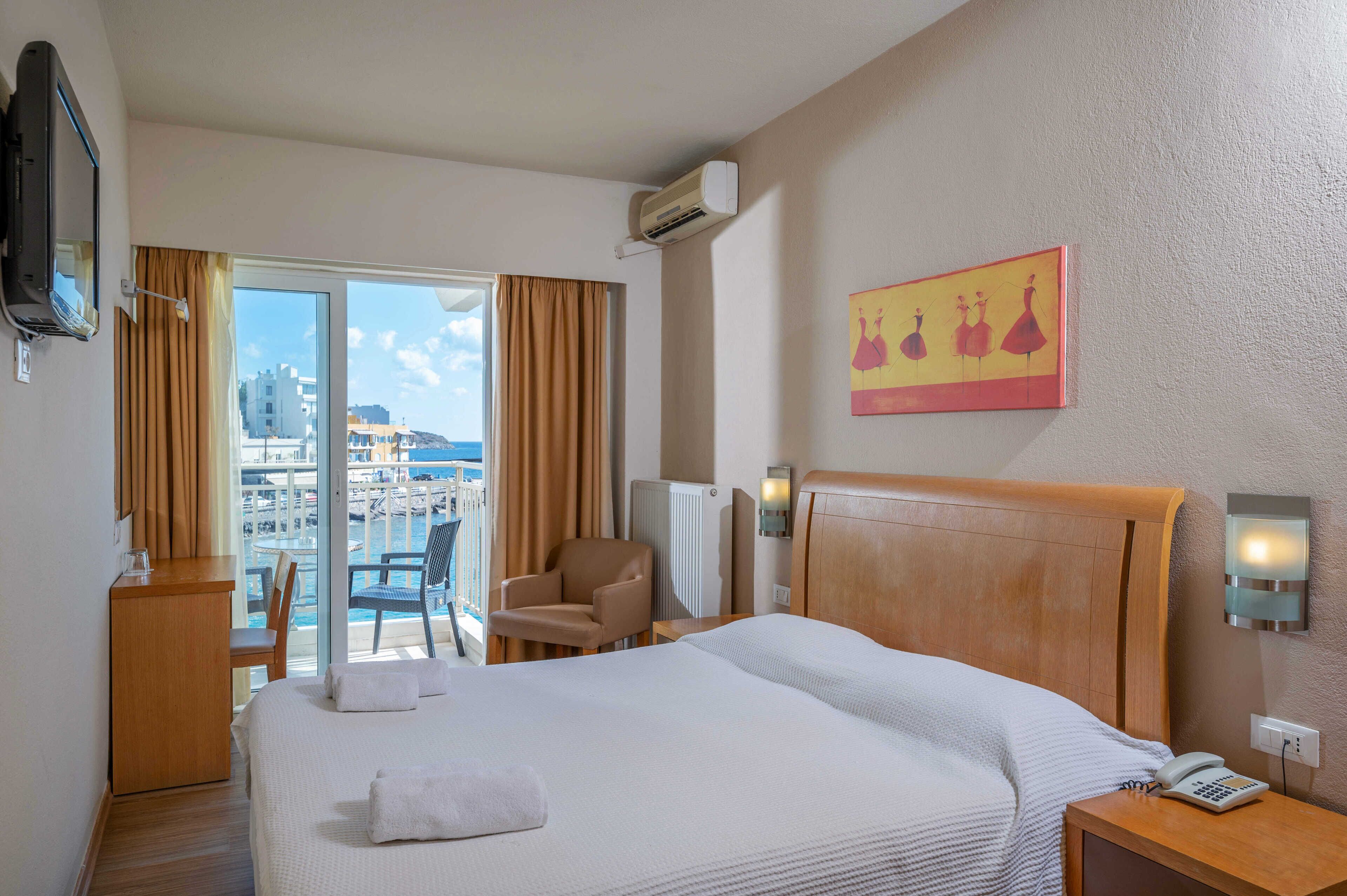 Habitación de hotel con una cama grande, un escritorio, una silla, un balcón con vista a la ciudad y un cuadro en la pared.