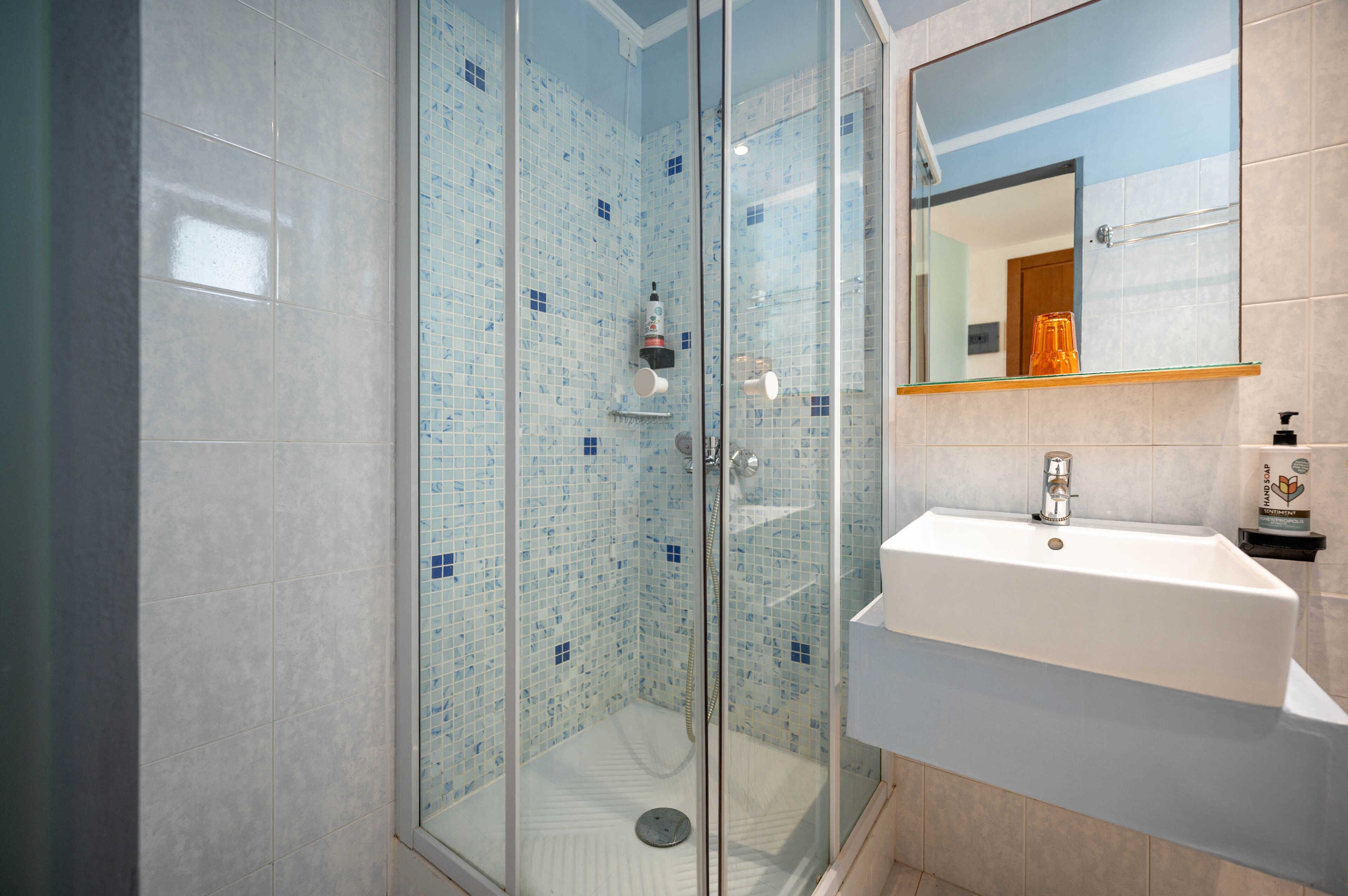 Un baño moderno con ducha envuelta en vidrio, un lavamanos blanco y un espejo sobre él.