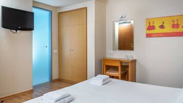 Habitación de hotel con cama, armario de madera, una mesita pequeña con espejo y televisor montado en la pared.