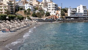 Una playa con sombrillas, costa rocosa y edificios al fondo.