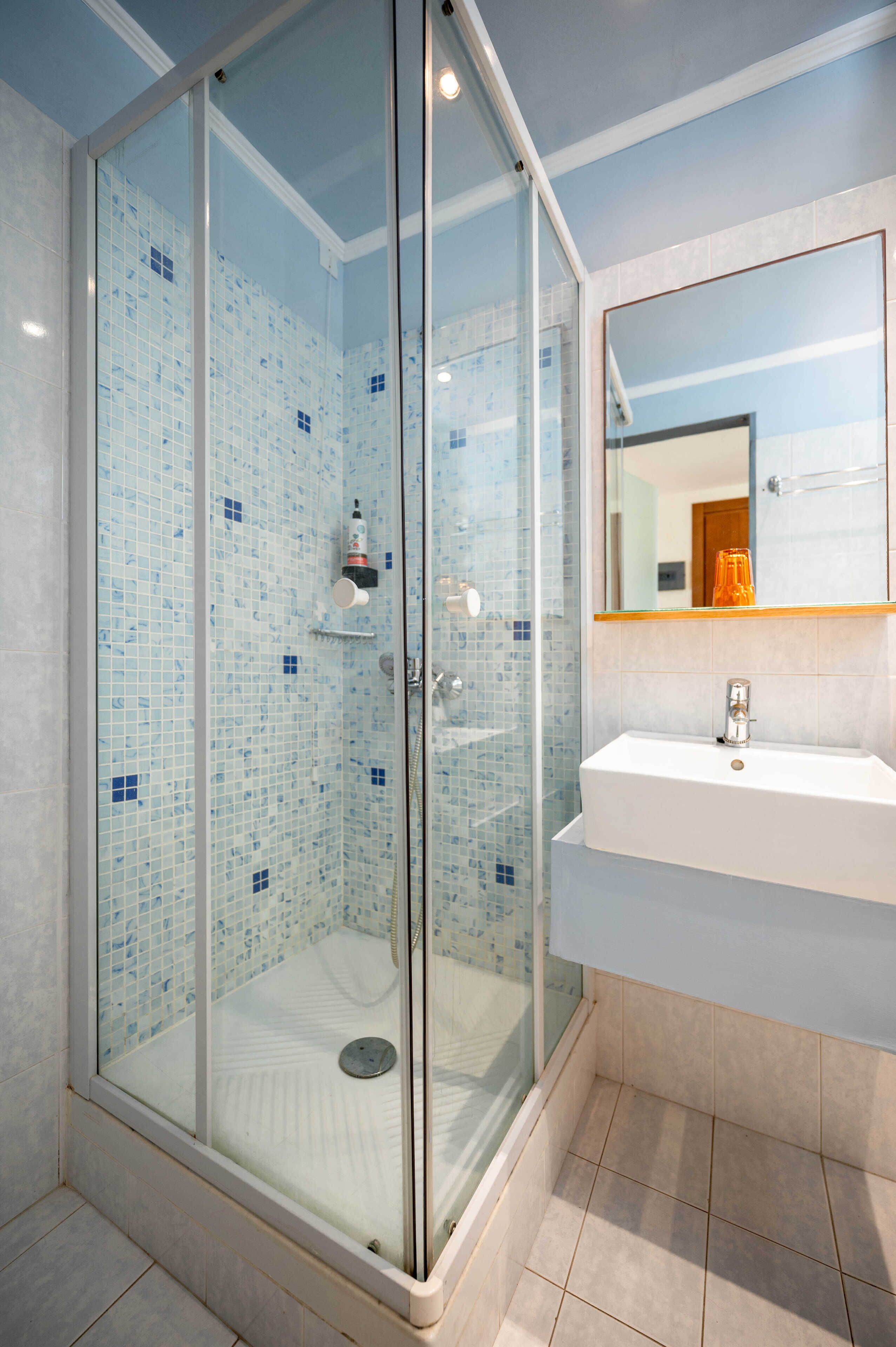 Une salle de bain moderne avec une douche à parois de verre, un lavabo blanc et un miroir au-dessus.
