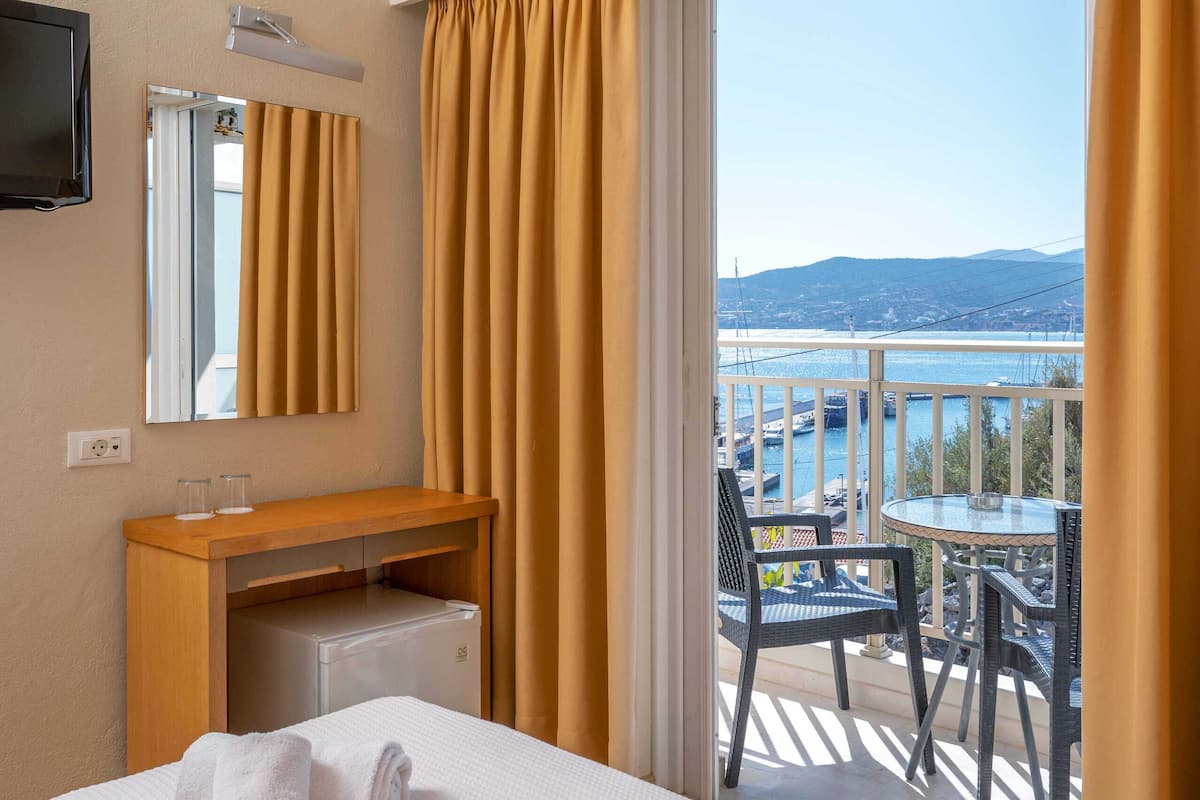 Ein Hotelzimmer mit Bett, einem Holztisch, einem Spiegel und Blick auf einen Balkon mit Tisch und Stühlen.