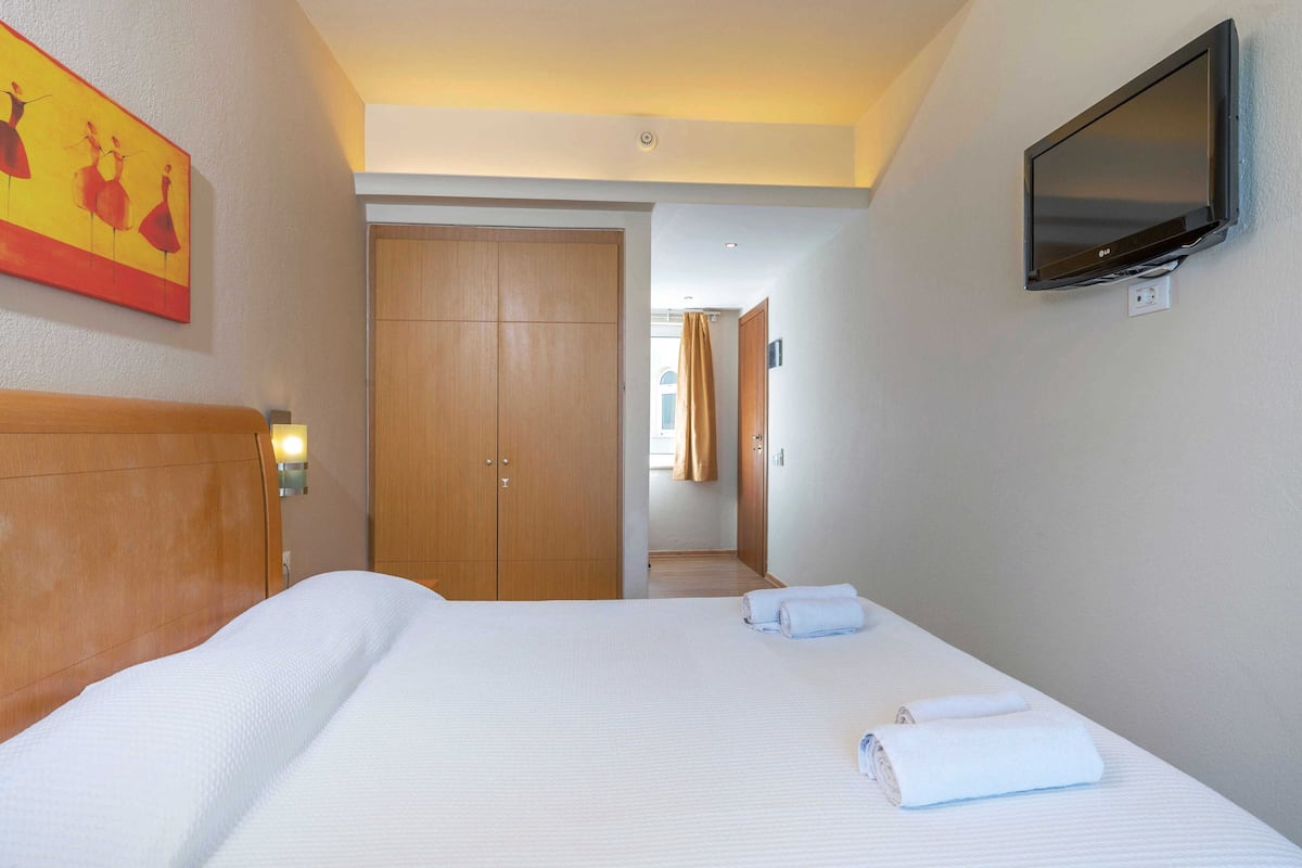 Ein Hotelzimmer mit einem Bett, einem an der Wand befestigten Fernseher und einem Holzschrank.
