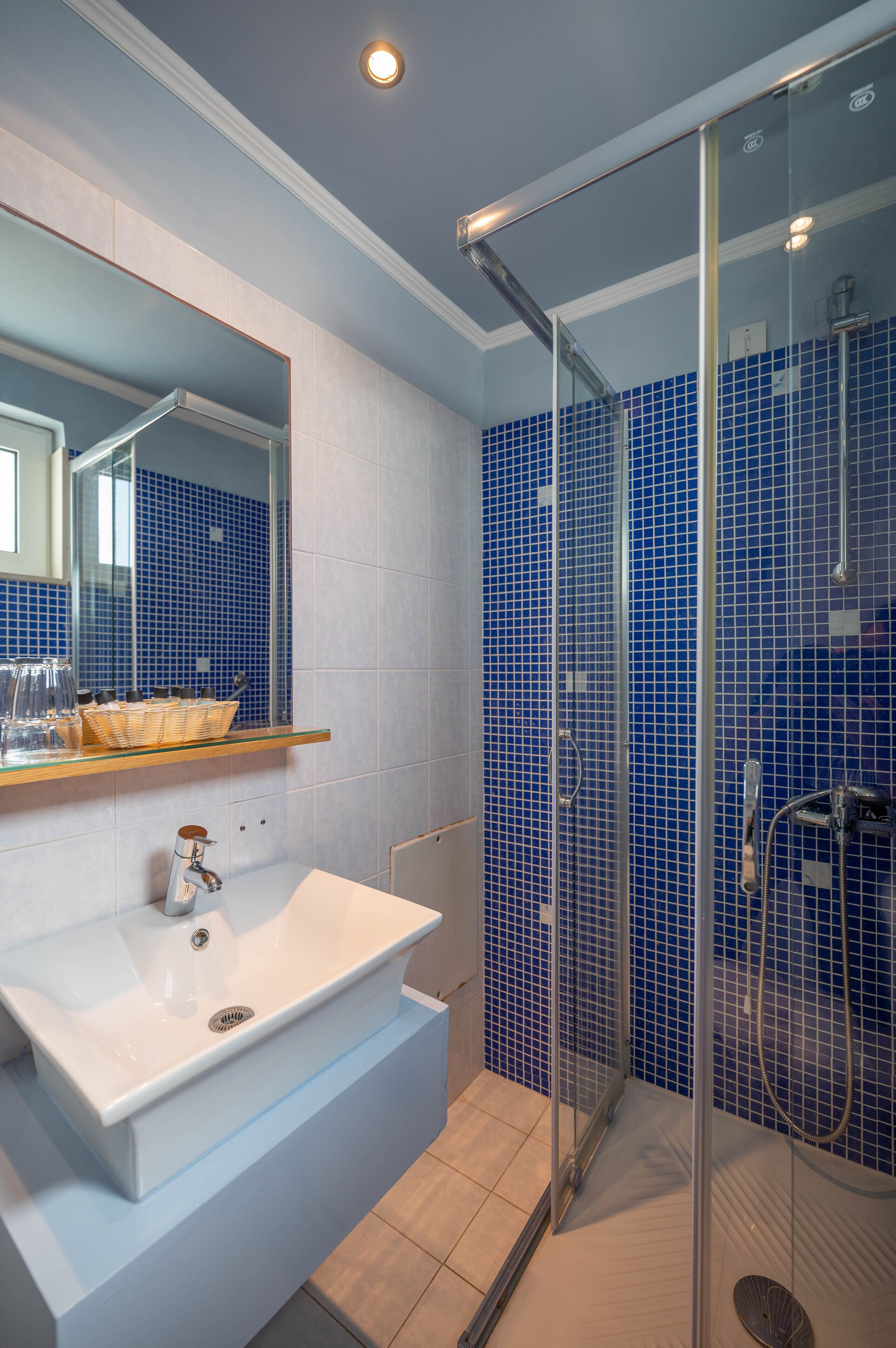 A modern bathroom with a white sink, a glass shower enclosure, and blue-tiled walls.