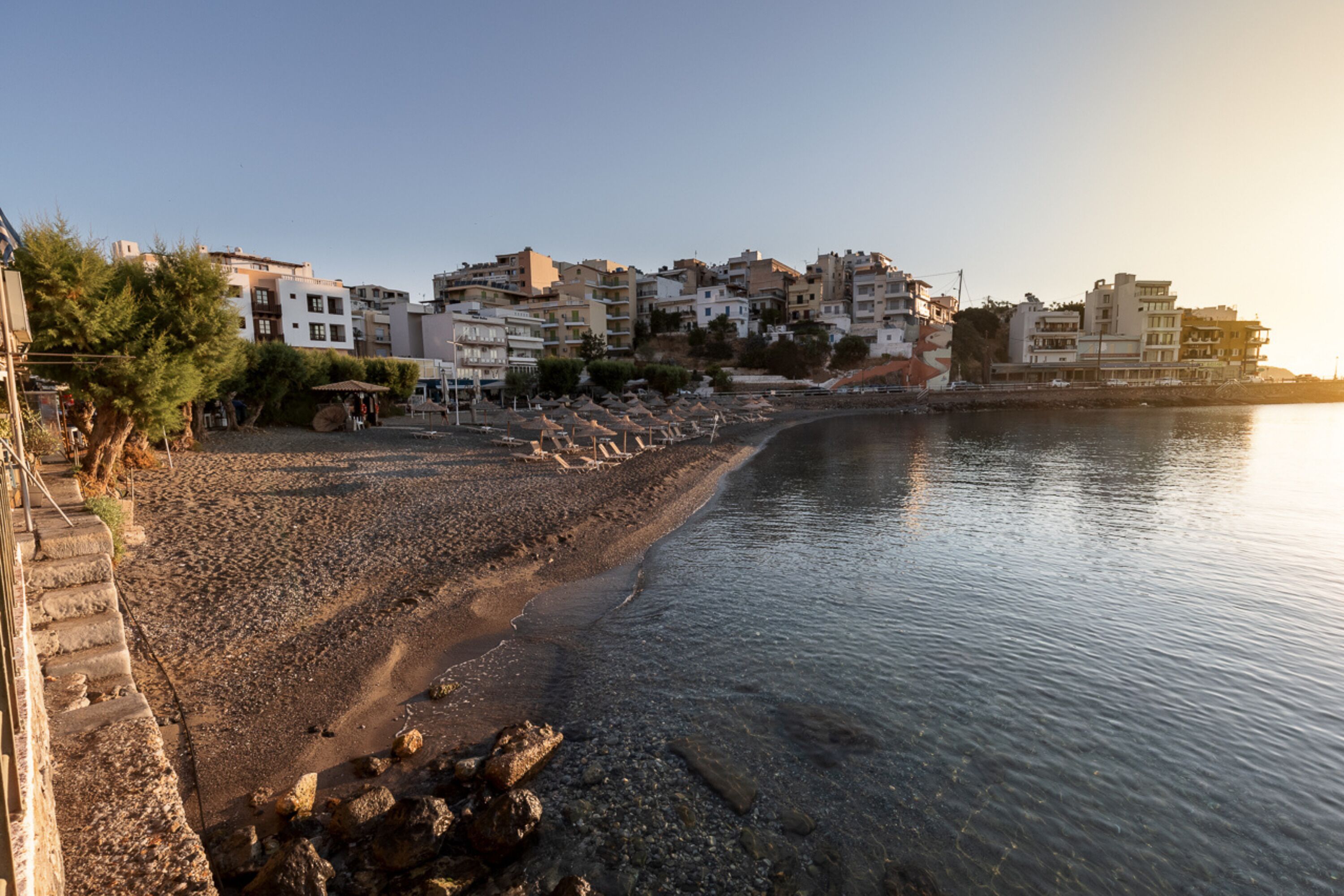 Une ville côtière avec des bâtiments qui bordent la plage, une plage de galets et une mer calme.