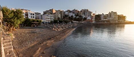 Une ville côtière avec des bâtiments qui bordent la plage, une plage de galets et une mer calme.