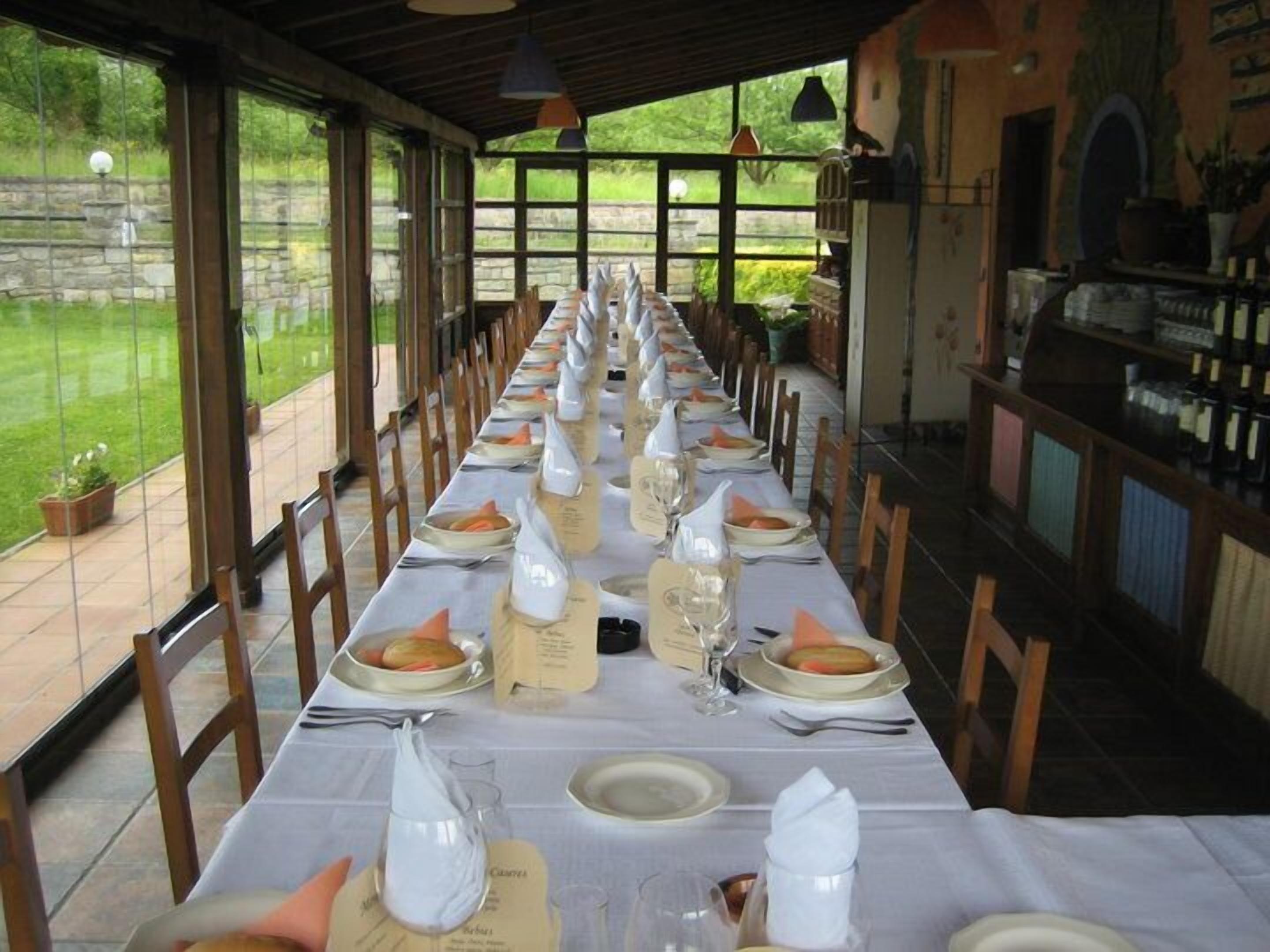 Una larga mesa de comedor lista para una comida, con manteles blancos, platos y vasos.
