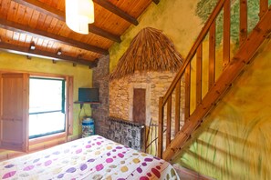 A bedroom with a bed, a stone wall, a wooden staircase, and a window. - Hotel Costa de Rodiles (Villaviciosa)