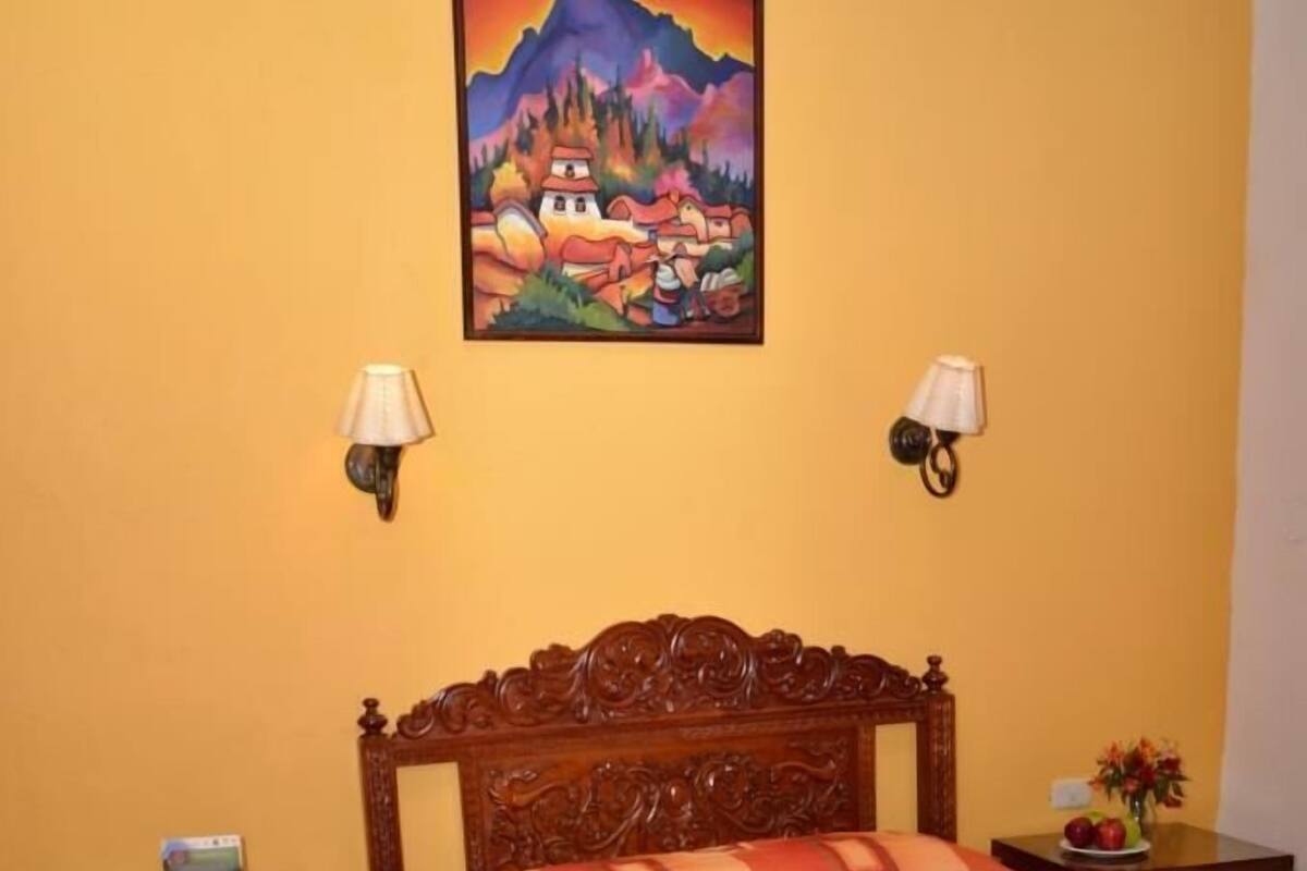 A bedroom with a wooden bed, a painting on the wall, two bedside lamps, and a nightstand with a lamp.