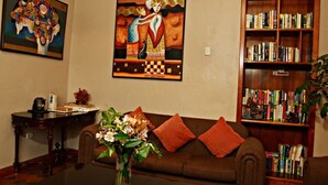 A living room with a brown sofa, a coffee table with a vase of flowers, a bookshelf filled with books, and two paintings on the wall. - Mallqui Hostal (Cusco)