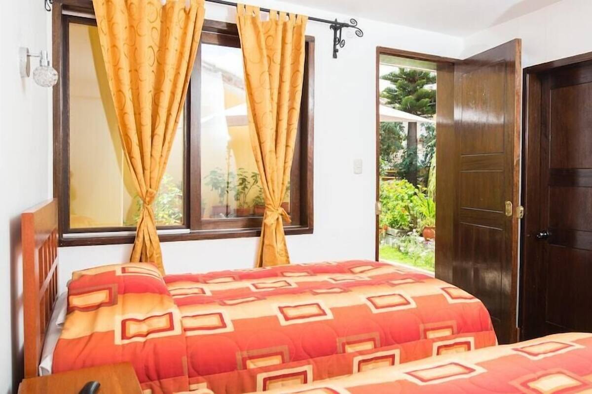 A bedroom with a bed, curtains, a window, a door, and a small table.