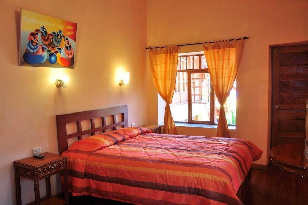 A bedroom with a bed, a nightstand, a painting on the wall, and a window with curtains.