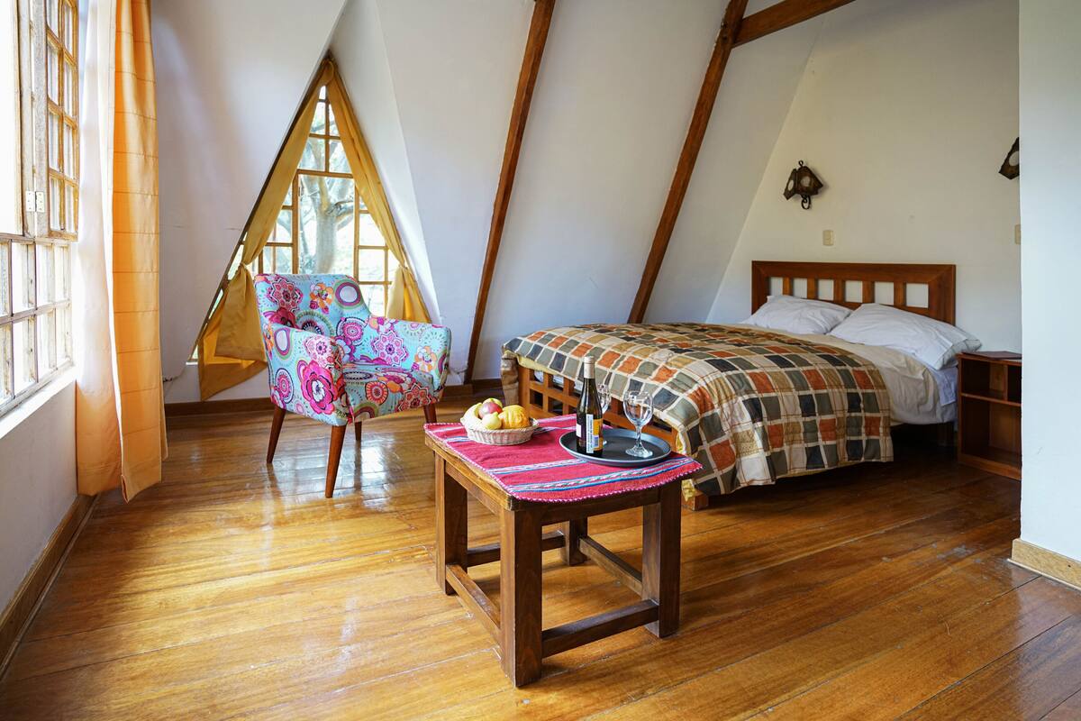 Un dormitorio acogedor con una cama de madera, una mesita con una bandeja de frutas y un vaso, y una silla colorida.