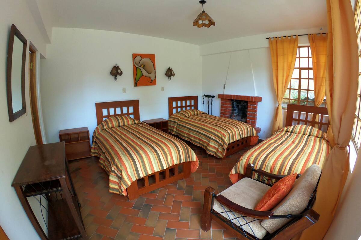 Una habitación con tres camas, una silla de madera, una chimenea y una lámpara en el techo.