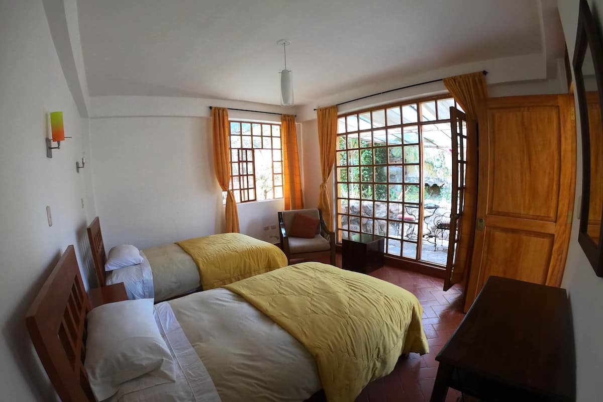 Una habitación con dos camas, una silla, una mesa y un ventanal con cortinas.