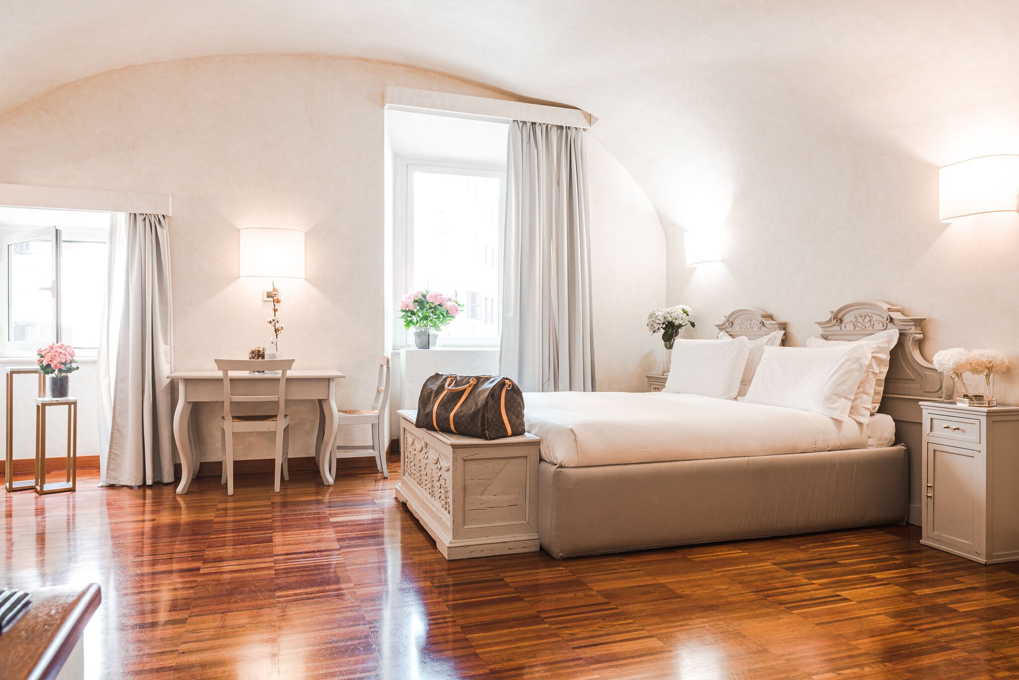 A bedroom with a bed, bedside table, lamp, desk, chair, and a window with curtains.