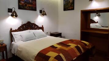 A neatly made bed with a patterned blanket, two wall-mounted lamps, and two paintings on the wall.