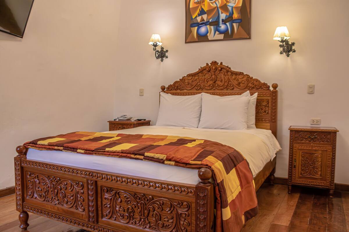 A wooden bed with a quilt, two wall sconces, and a painting above.
