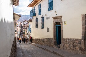A narrow cobblestone street lined with buildings featuring stone bases and blue shutters.