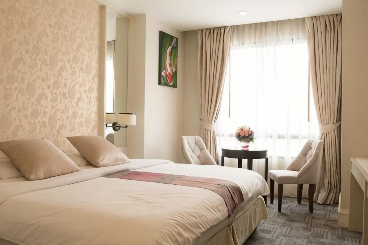 Une chambre d’hôtel avec un grand lit, deux fauteuils, une petite table ornée de fleurs et une fenêtre avec des rideaux.