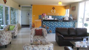 A hotel lobby with floral armchairs, a brown leather sofa, a reception desk, and a tiled wall with a 'C2 Residence' sign. - C2 Residence Boutique Hotel (Lampang)
