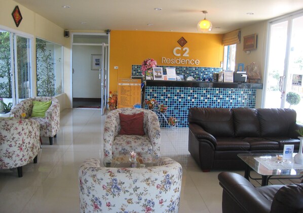 A hotel lobby with floral armchairs, a brown leather sofa, a reception desk, and a tiled wall with a 'C2 Residence' sign.