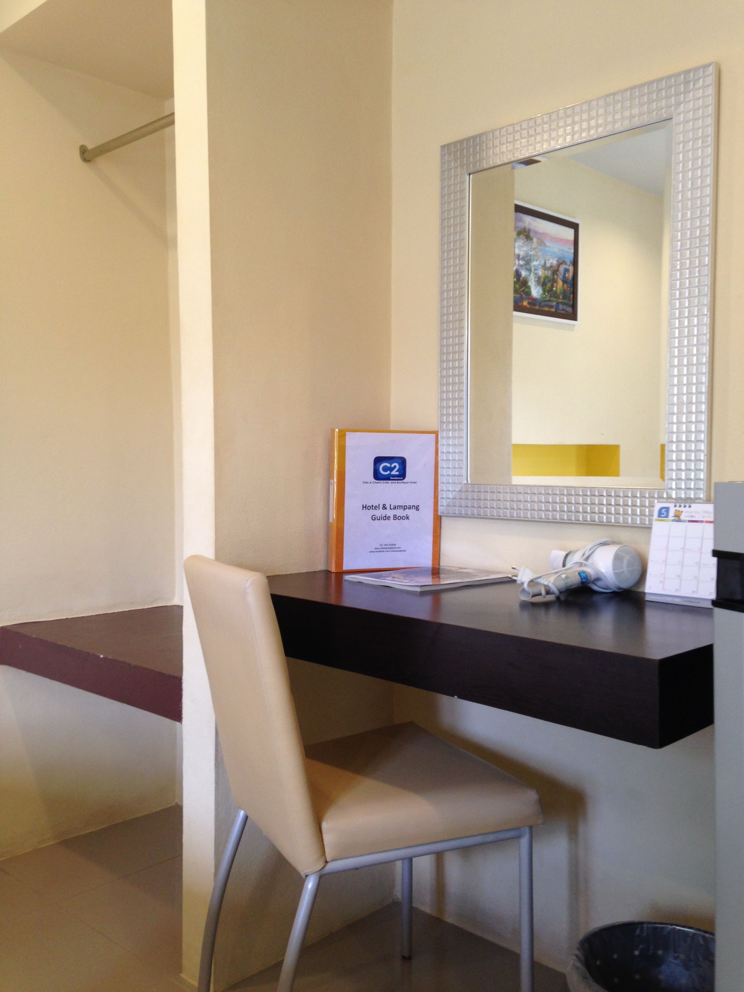 A hotel room with a desk, chair, and a mirror with a decorative frame. A guide book is placed on the desk.