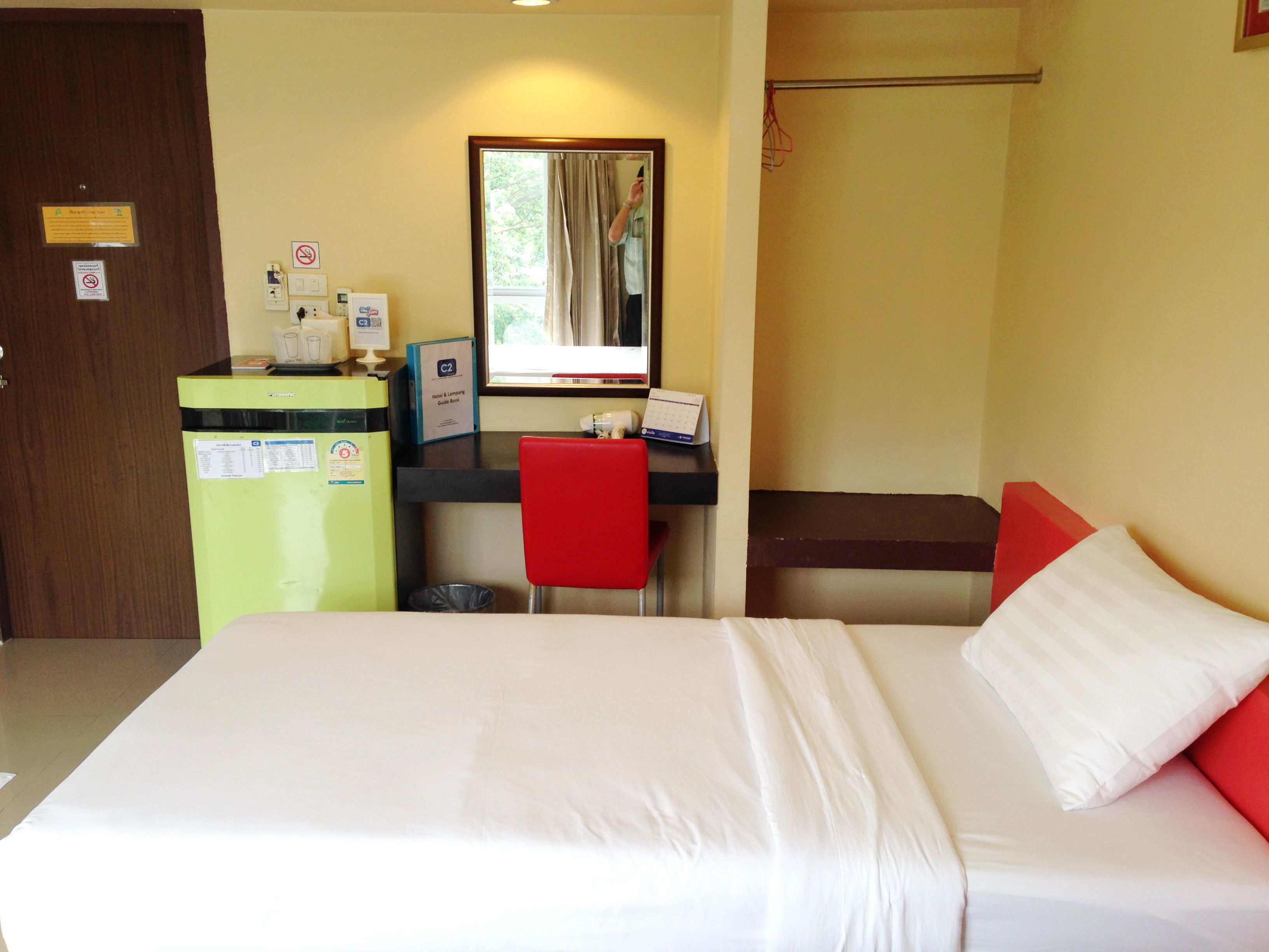A hotel room with a bed, a desk, a chair, a small trash bin, and a door.