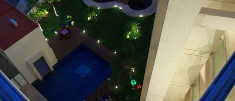 An aerial view of a courtyard with a swimming pool, surrounded by greenery and illuminated by string lights.