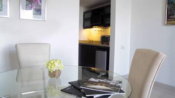 A modern dining area with a glass table, two chairs, a vase with flowers, and framed pictures on the wall.