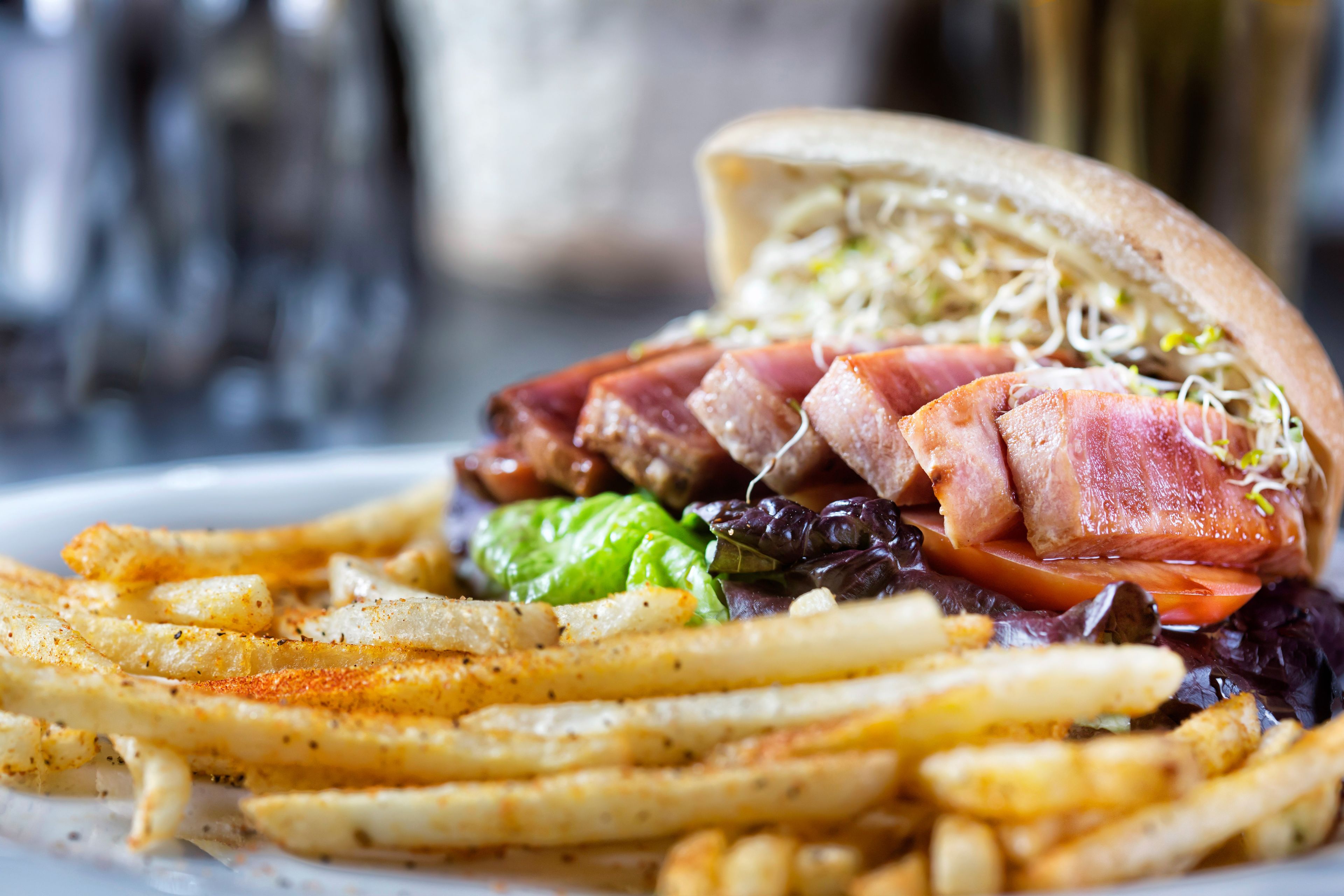 A sandwich with meat, lettuce, and tomato on a bun, accompanied by French fries.