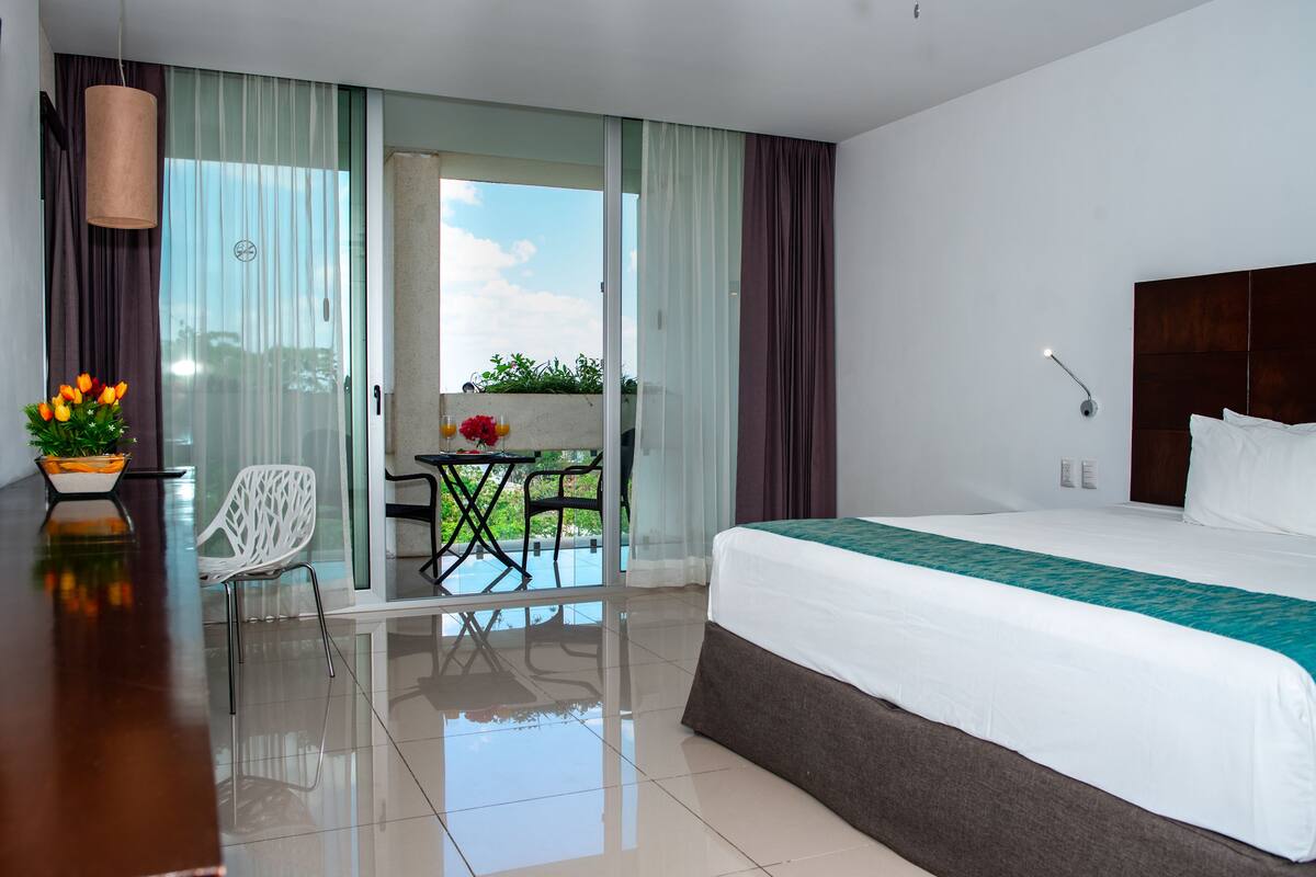 Una habitación de hotel con cama, escritorio, silla y balcón con mesa y sillas.