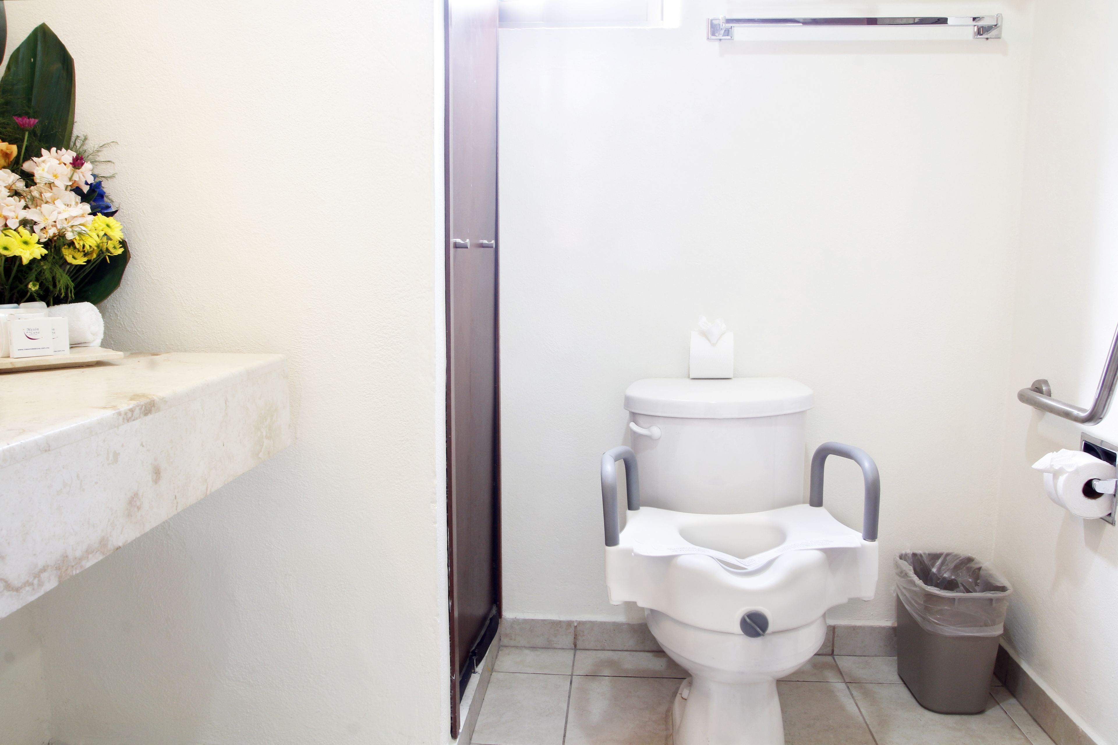 A small bathroom with a toilet, a trash can, and a sink with a towel dispenser.
