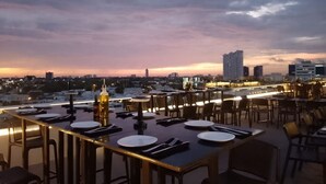 Un restaurant situé sur un toit, avec des tables dressées pour le dîner, offrant une vue sur le paysage urbain au crépuscule.