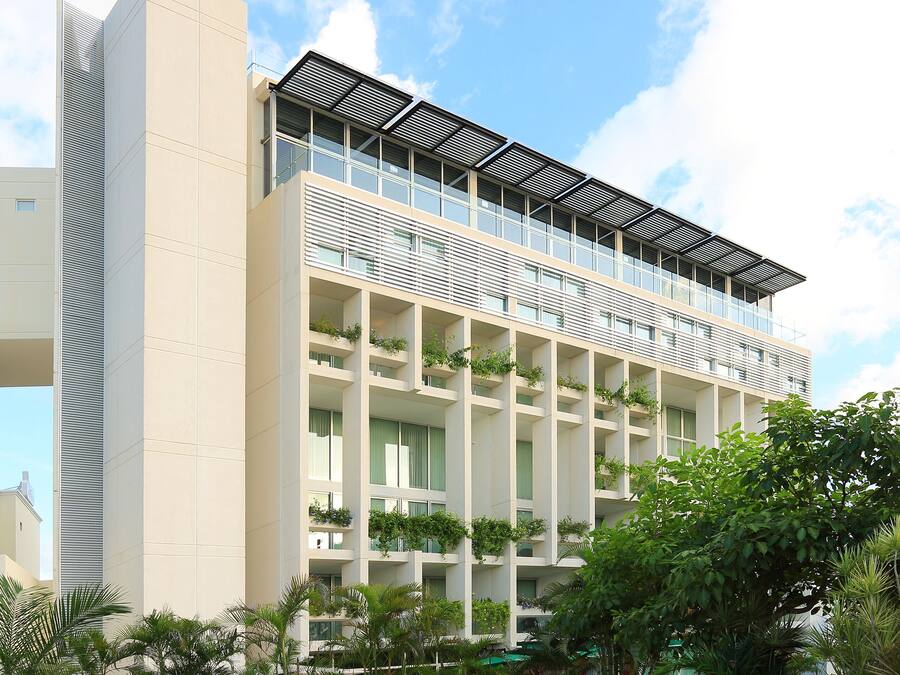 Un hotel moderno con techo plano, varios balcones y un jardín con un puente y asientos.