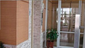 A hotel entrance with a wooden door, a potted plant, and a view of the street outside. - Thanaplace Jaran 34 (Bangkok)