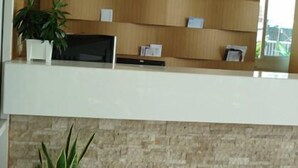 A reception desk with a wooden panel wall, a potted plant, and a stone wall below. - Thanaplace Jaran 34 (Bangkok)